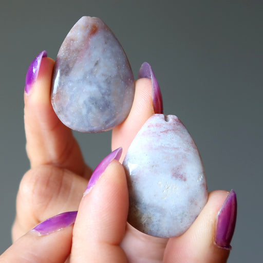 Hand holding two teardrop-shaped stones with a blurred gray background