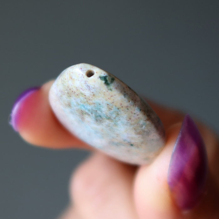 Hand holding a small stone with a dark gray background