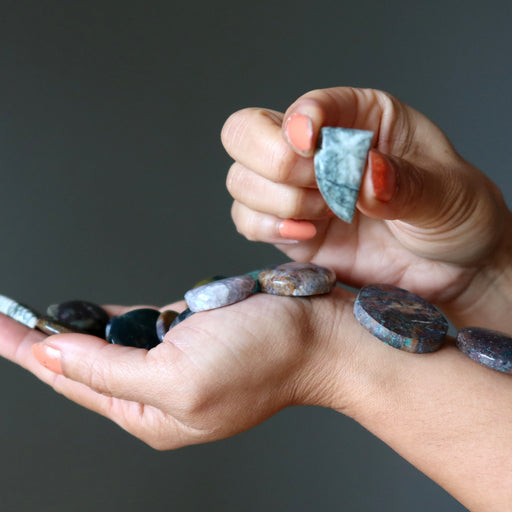 Hands holding and displaying various stones against a dark background