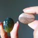 Two hands holding a green and brown stone against a dark background