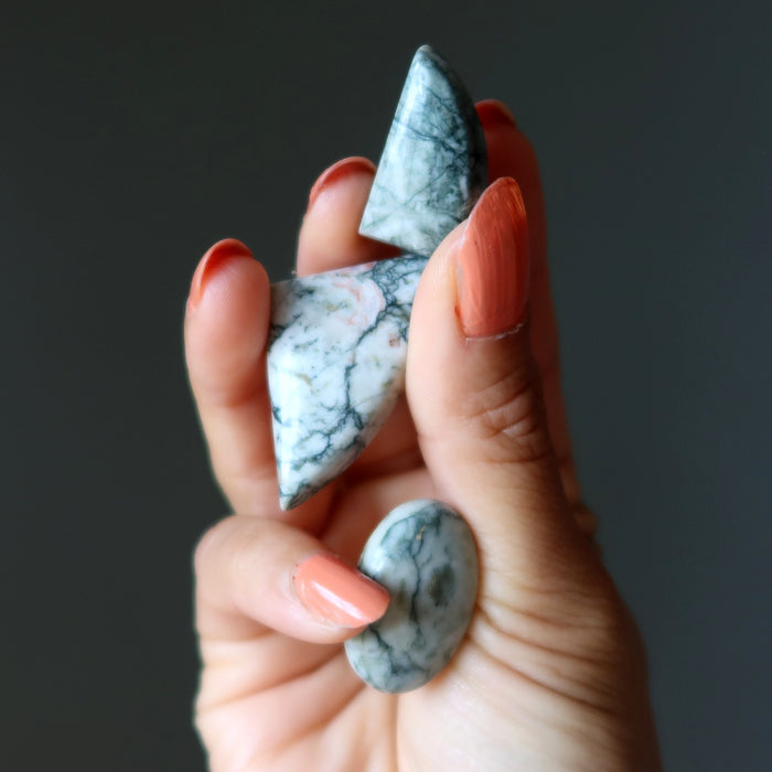 Hand holding three marbled stones against a dark background