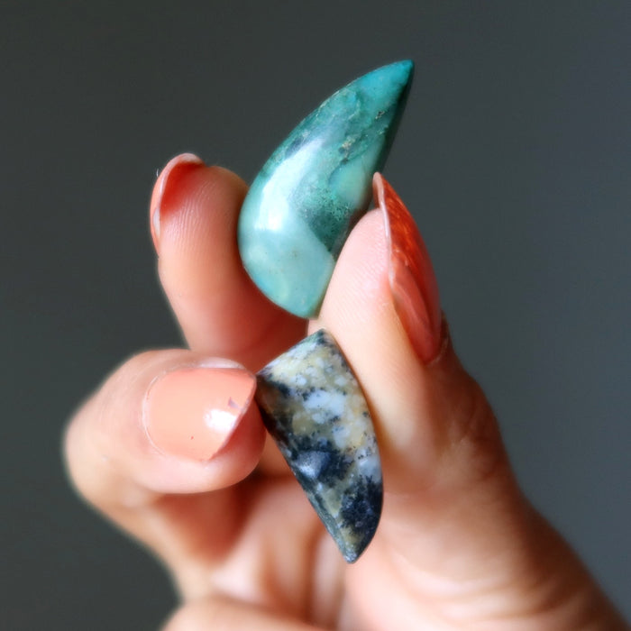 Hand holding two turquoise stones against a dark background