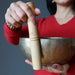 Person holding a gold singing bowl with a wooden handle against a gray background