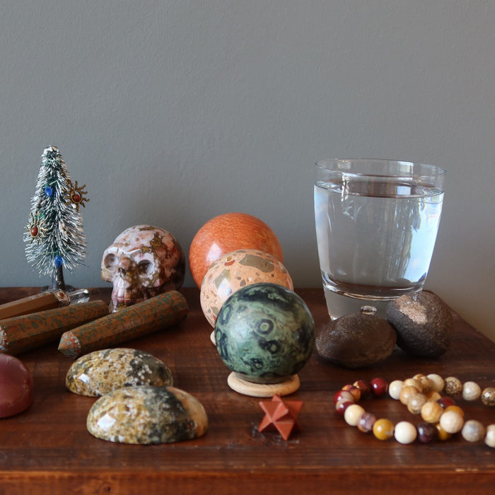 Collection of decorative items including stones, a glass of water, and a small tree on a wooden surface.