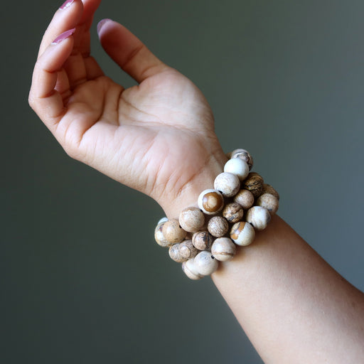 Hand wearing a stack of beaded Landscape Jasper bracelets on a neutral background