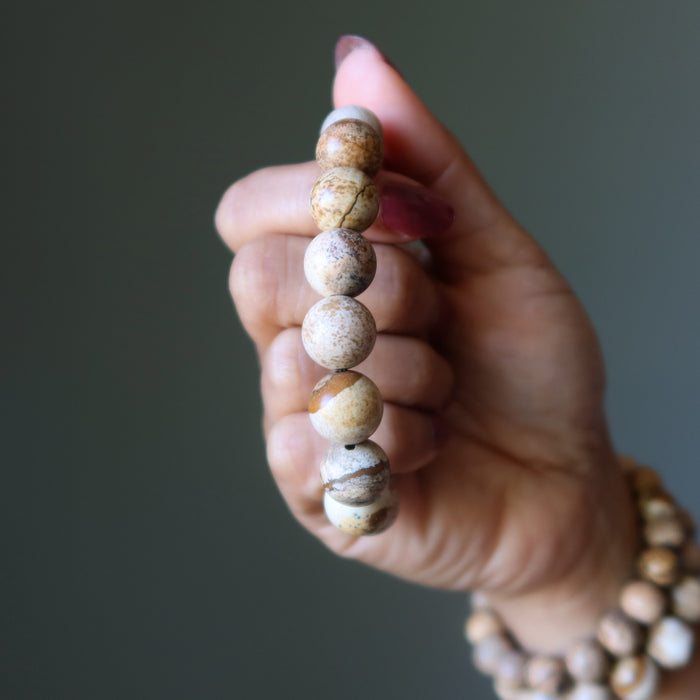 Hand holding a beaded Landscape Jasper bracelet against a neutral background