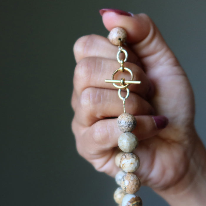 Hand holding a beaded Landscape Jasper necklace with gold accents against a dark background
