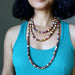 Woman wearing a turquoise tank top and multiple beaded mookaite jasper beaded necklaces with a neutral background