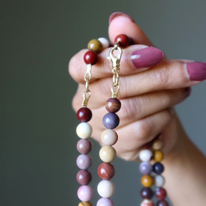 Hand holding a mookaite jasper beaded necklace with a neutral background