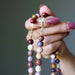 Hand holding a mookaite jasper beaded necklace with a neutral background