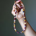 Hand holding a multicolored beaded mookaite jasper beaded necklace against a neutral background