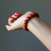 Hand wearing a red beaded bracelet against a gray background