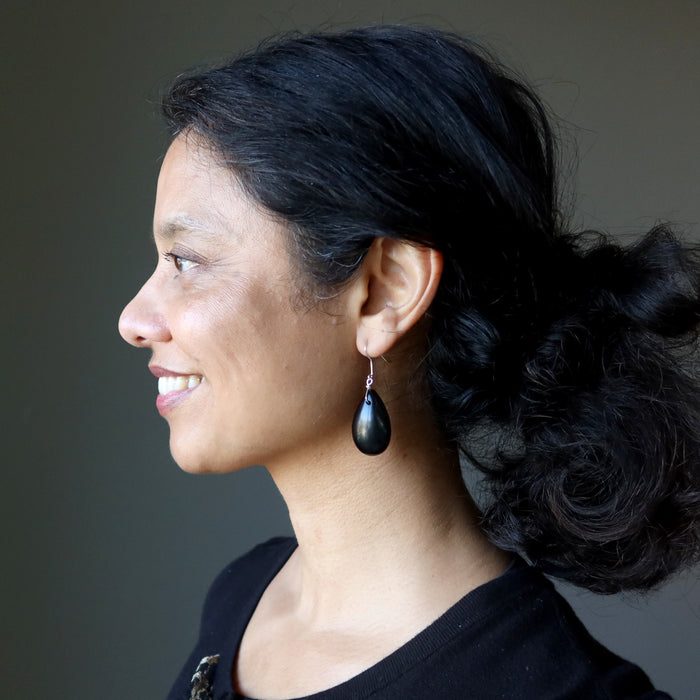 Woman with black hair and Jet earrings against a gray background