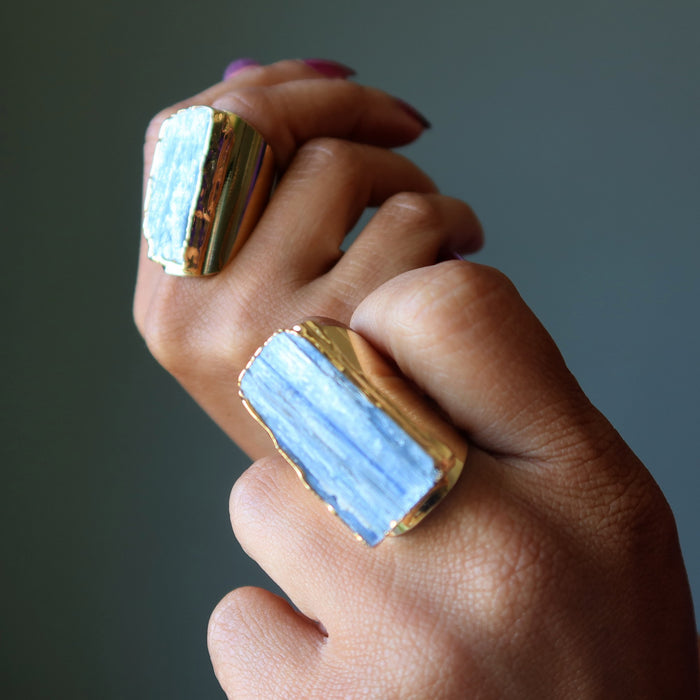 Hand wearing two gold and blue Kyanite rings on a dark background