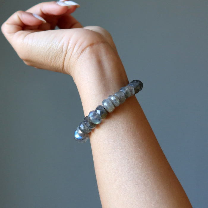 Hand wearing a Labradorite bracelet with gray beads on a neutral background