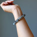 Hand wearing a Labradorite bracelet with gray beads on a neutral background
