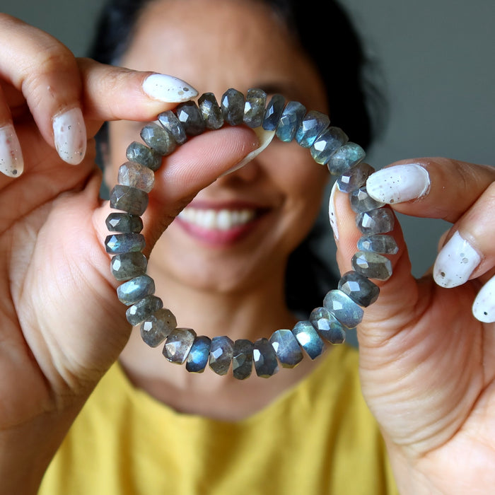 Person holding a Labradorite bracelet made of faceted gemstones, blurred background