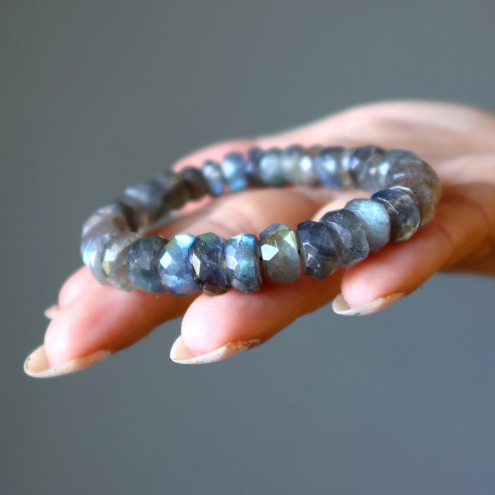 Hand holding a Labradorite bracelet against a neutral background