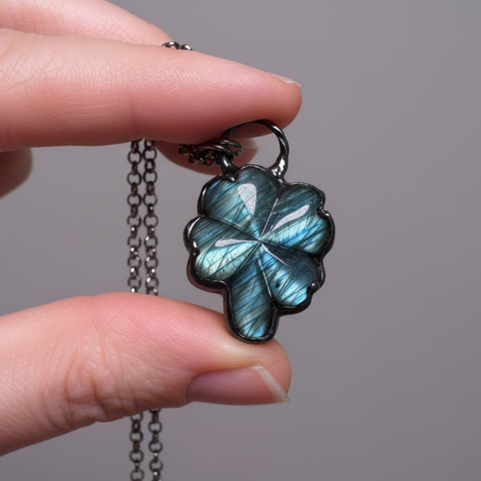 Hand holding a necklace with a leaf-shaped pendant 