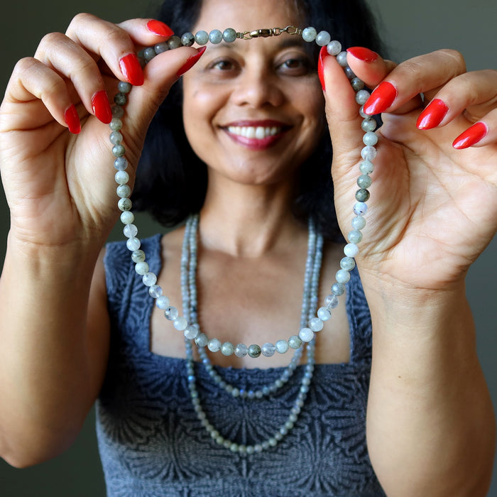 Woman holding a beaded Labradorite necklace with a neutral background
