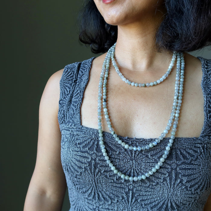 Woman wearing a patterned top and multiple beaded Labradorite necklace against a dark background