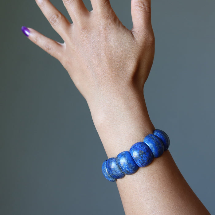 Hand wearing a blue beaded Lapis bracelet against a gray background
