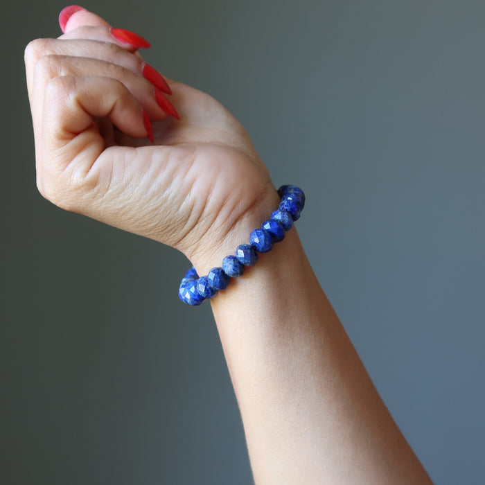 Hand wearing a blue beaded Lapis bracelet on a gray background