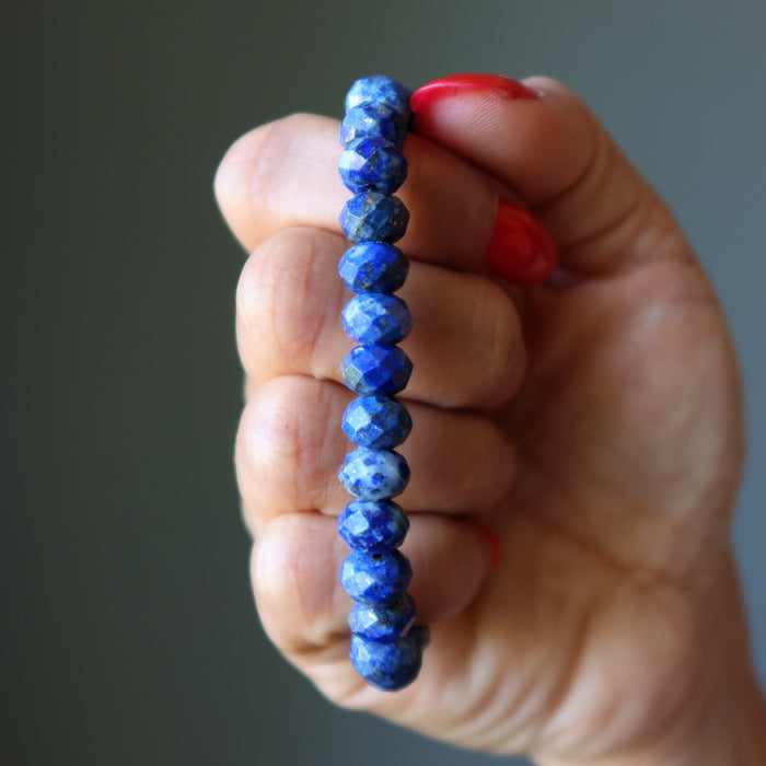 Hand holding a blue beaded Lapis bracelet against a neutral background