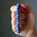 Hand holding a blue beaded Lapis bracelet against a neutral background