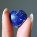 Hand holding a blue lapis stone against a gray background