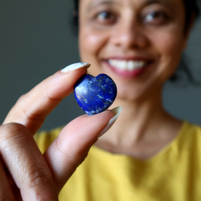 Person holding a blue lapis heart-shaped stone with a blurred background