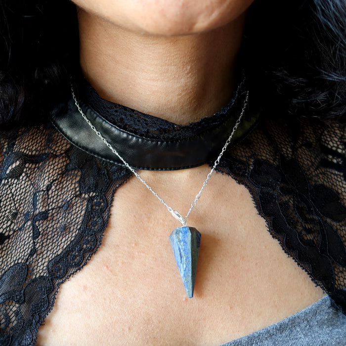 Person wearing a blue lapis pendant necklace with a black lace garment.