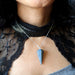 Person wearing a blue lapis pendant necklace with a black lace garment.
