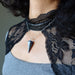 Person wearing a black lace garment with a necklace featuring a triangular lapis pendant.