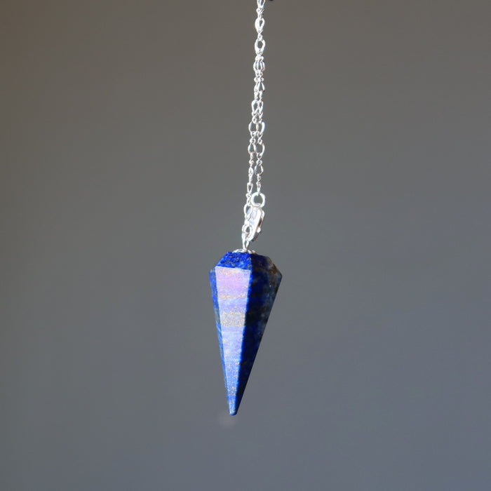 Blue lapis crystal pendulum on a chain against a gray background