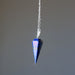 Blue lapis crystal pendulum on a chain against a gray background