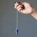 Hand holding a blue lapis crystal pendulum against a gray background