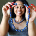 Woman holding a blue beaded Lapis Lazuli necklace with a plain background