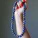 Hand holding a blue beaded Lapis Lazuli necklace against a gray background