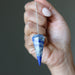 Hand holding a blue and white crystal lapis pendulum against a neutral background