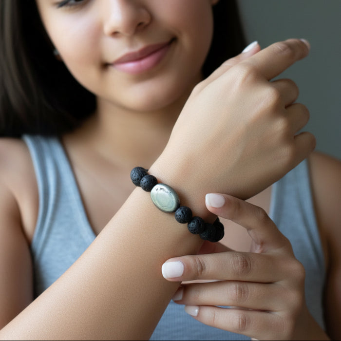 Hand wearing lava beaded bracelet with a central pyrite bead on a gray background