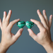Two hands holding two green malachite heart-shaped stones against a gray background