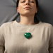 Woman wearing a beige sweater with a green malachite heart on chest  against a dark background