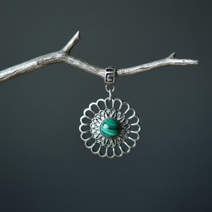 Silver pendant with a green malachite stone on a branch against a dark background