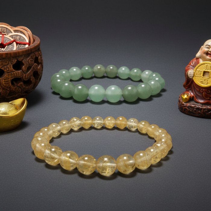 citrine and aventurine bracelets on a dark surface with a small statue and gold ingot.