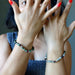 Close-up of hands with red nail polish wearing beaded bracelets on a neutral background