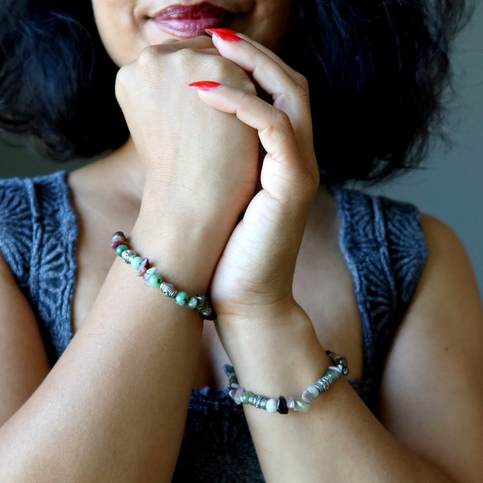 Close-up of a person's hands with bracelets, wearing a gray sleeveless top.