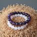 Two beaded bracelets, one amethyst purple and one rose quartz pink, on a bed of rice.
