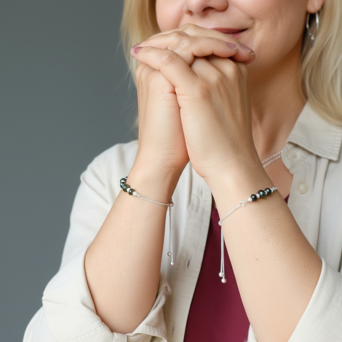 Woman with hands clasped wearing beaded moldavite bracelets on a neutral background
