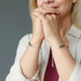 Woman with hands clasped wearing beaded moldavite bracelets on a neutral background